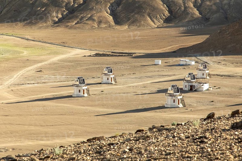 A series of small observatory structures dot the isolated, vast arid plains of Ladakh, India, under the harsh sun and clear blue skies, capturing the serenity and openness of the landscape