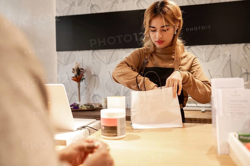 A cosmetics store worker assisting a customer, packing products in a bag. The modern store interior features subtle decor, creating a welcoming shopping experience