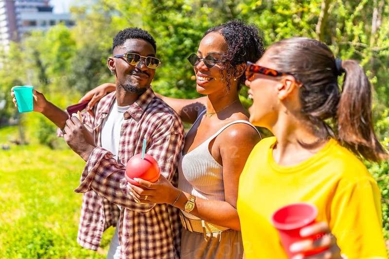 Three friends are walking through a park, enjoying drinks and each other's company on a sunny day