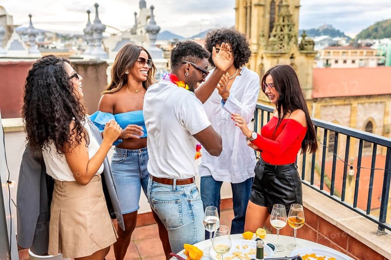 Multiracial friends dancing happily during tropical party in a rooftop with city views during sunset