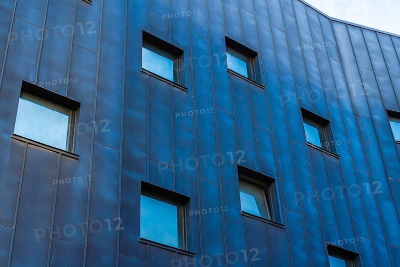 A contemporary building showcasing a multicolored facade, emphasized by a pattern of blue-tinted metallic panels, punctuated by rectangular windows
