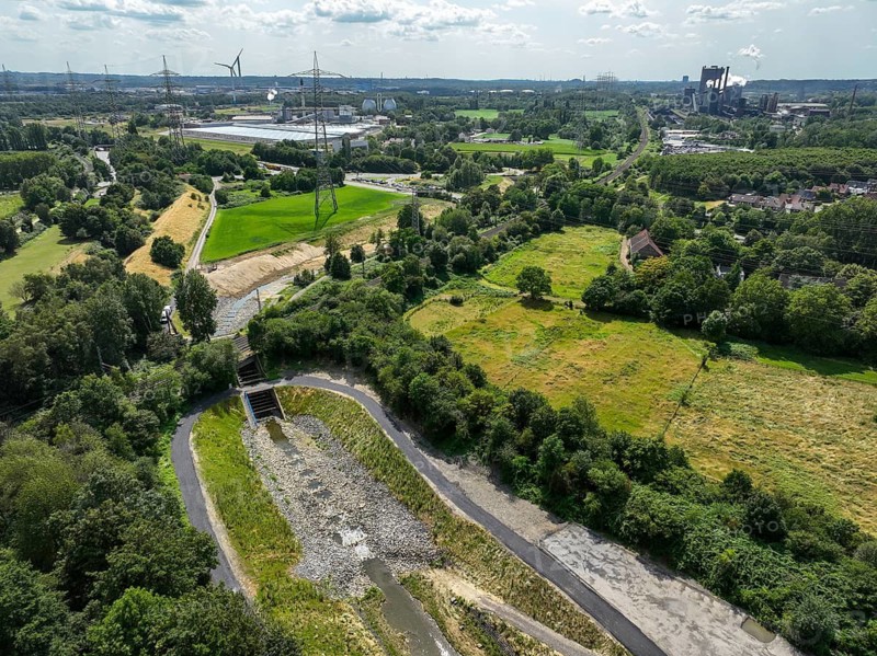 Bottrop, North Rhine-Westphalia, Germany, Renaturalised Boye in the Ruhr industrial landscape, the tributary of the Emscher was transformed into a near-natural watercourse, flood protection through newly designed flooding areas, the Boye is now free of wastewater after the construction of a parallel sewer, is part of the Emscher river system and thus part of the Emscher conversion, was previously an open, above-ground wastewater canal, mixed water canal with surface water and wastewater. Coking plant Prosper, ArcelorMittal Bottrop, at the back right. Rear left Bottrop wastewater treatment plant, Emschergenossenschaft
