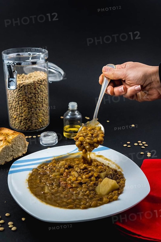 A spoon inside a plate of Spanish cooked lentils