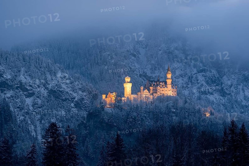 Snow-covered castle, illuminated at dusk, embedded in misty mountains, Neuschwanstein, Schwangau, Ostallgäu, Allgäu, Swabia, Upper Bavaria, Bavaria, Germany