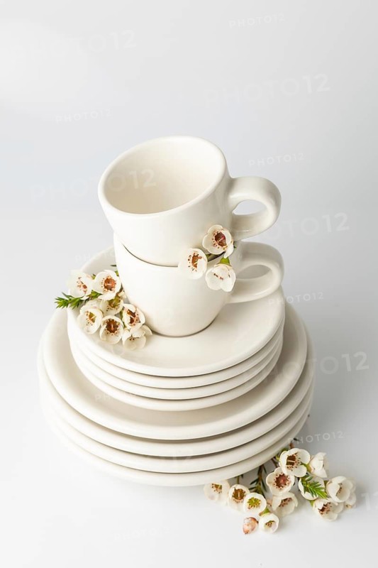 Neatly arranged spring tableware set featuring stacked white ceramic plates and cups, each adorned with delicate cherry blossoms. The soft blossoms add a touch of spring aesthetic to the minimalist design, highlighting an elegant home decor theme