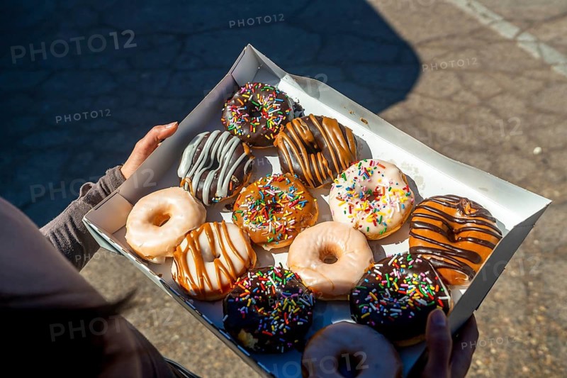 Person holding an open box filled with a variety of sweet donuts, featuring different flavors of icing, sprinkles, and glazes, creating a tempting display of popular desserts for sharing