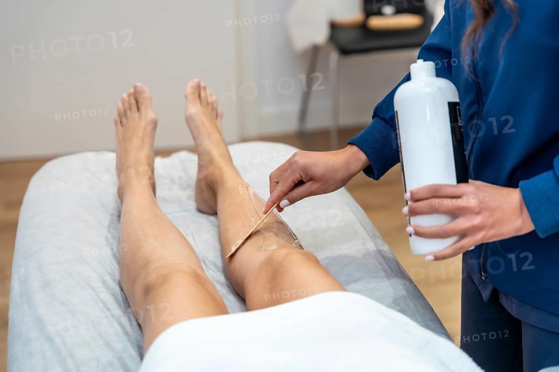 Woman lying on a salon bed, receiving professional hair removal treatment on her leg, with an aesthetician applying cooling gel for skin care and depilation