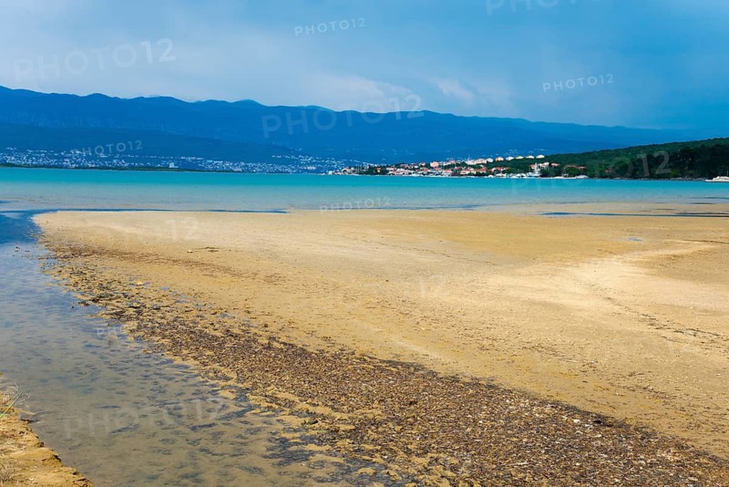 Wide beach landscape with watercourse, mountains in the background and a village along the coast under a cloudy sky, salty healing mud, Soline bay, Klimno, Krk island, Primorje-Gorski kotar, Croatia