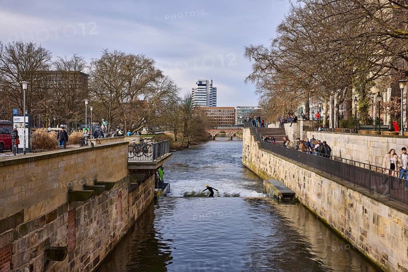 Leine wave, river Leine, footpath, bare wintry trees, lanterns, general architecture, high-rise building, artificial wave, wave surfing, pedestrians as accessories, diffuse light, milky blue cloudy sky, slightly sunny, Am Hohen Ufer, Leibnizufer, Mike-Gehrke-Promenade, Hanover, state capital, Hanover region, Lower Saxony, Germany
