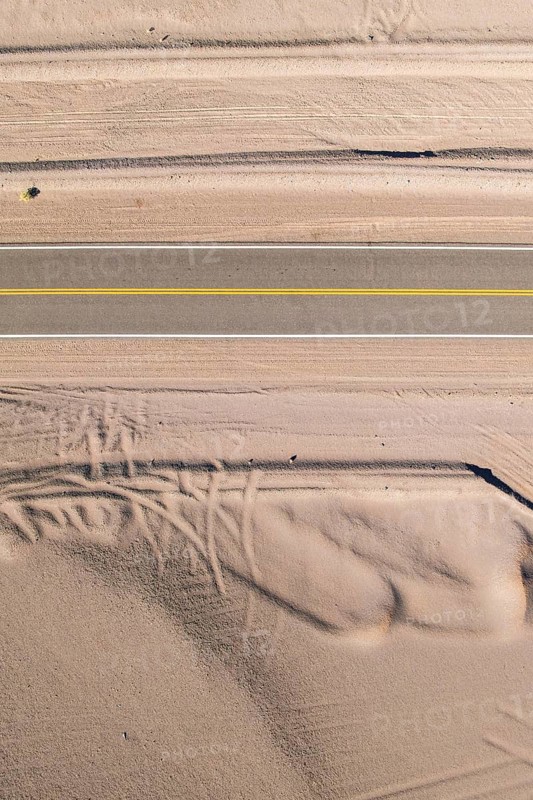 Aerial view of a straight asphalt road cutting through a sandy desert landscape of the argentine Puna. The road is accompanied by intricate patterns in the surrounding sand, formed by natural forces