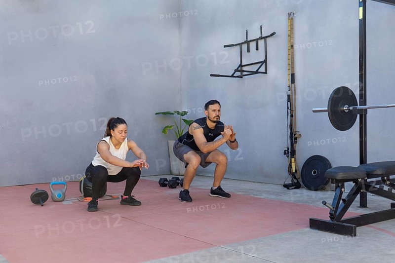 Two fitness professionals demonstrating proper squat technique in a modern outdoor gym, emphasizing strength and flexibility training while promoting a healthy and active lifestyle