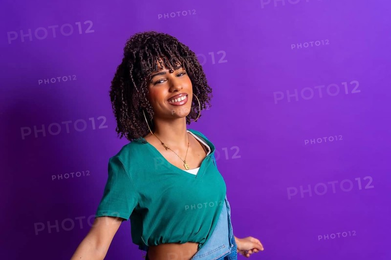 Carefree young latin woman with curly hair dancing, wearing a green t shirt and denim jacket on a vibrant purple background