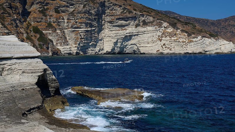 Whipped waves break on limestone rocks with boat in the blue sea, white volcanic strata, bizarre white rocks in the sea, Little Sarakiniko, Kioni Beach, Kioni, Kimolos Island, Cyclades, Greek Islands, Greece