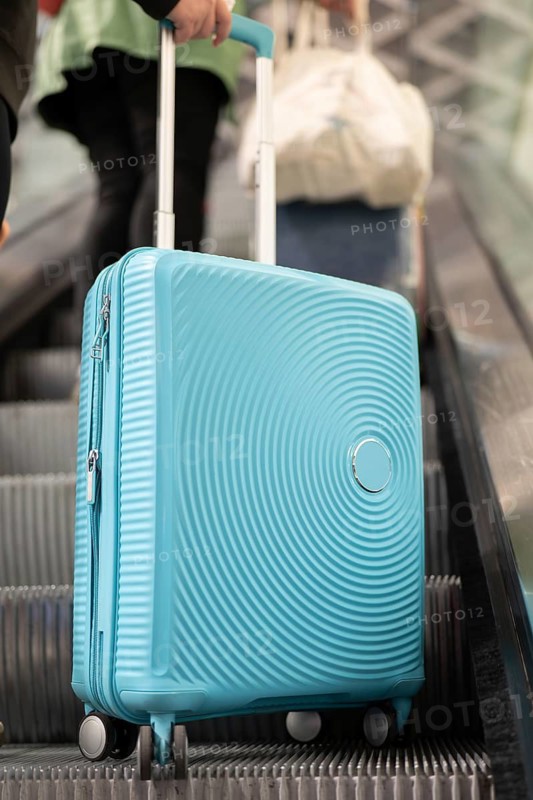 A traveler ascends an airport escalator with a stylish blue suitcase. The image captures a common travel scene, emphasizing the dynamics of modern transportation