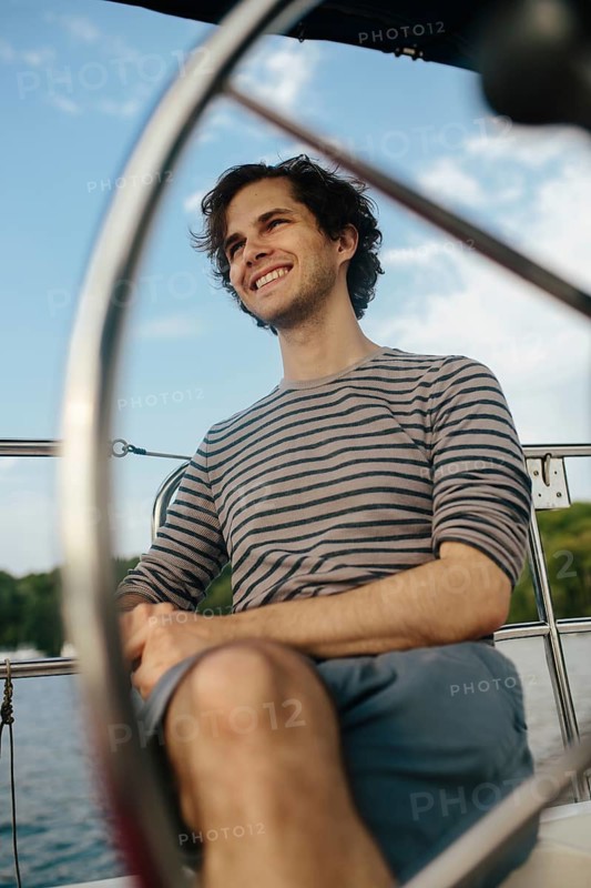 A man enjoys a serene afternoon on a sailboat. The scene captures a relaxed mood with a backdrop of blue skies and calm waters, embodying a perfect sailing day