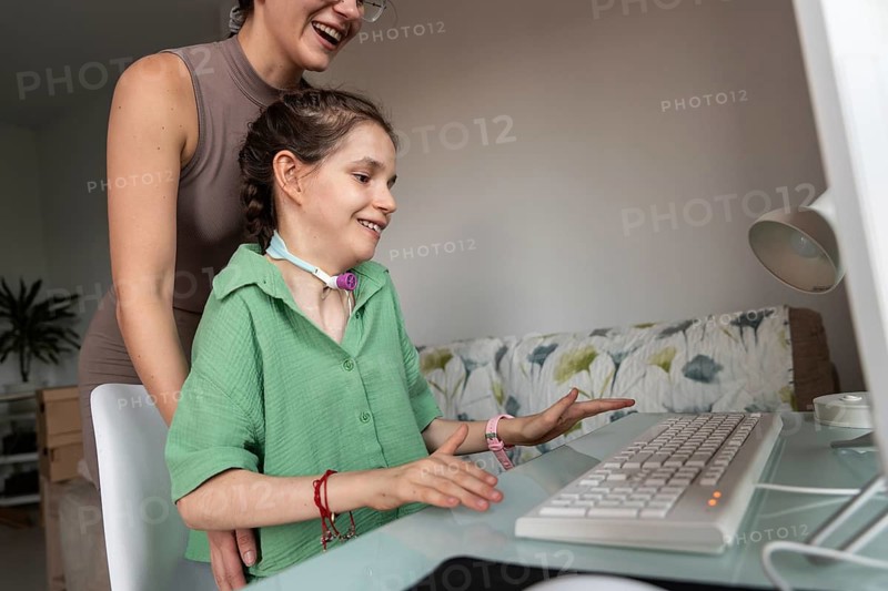 A heartwarming scene captures a sister supporting a disabled girl with tracheostomy. She smiles while using a computer, highlighting resilience and love