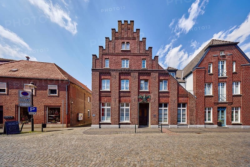 Historic city center, historic brick building Schwarzer Adler, façade with windows, staggered gable, barrier bollard, street, paving stones, blue sky, cumulus clouds, Feldstraße, Wachtendonk, Kleve district, North Rhine-Westphalia, Germany