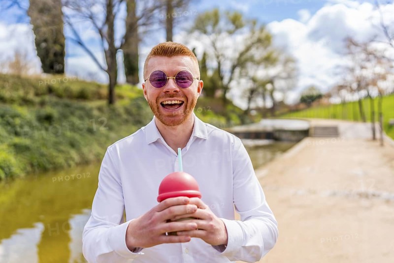 Cheerful businessman enjoying a refreshing smoothie in a park, soaking up the sun and savoring a relaxing break amidst nature