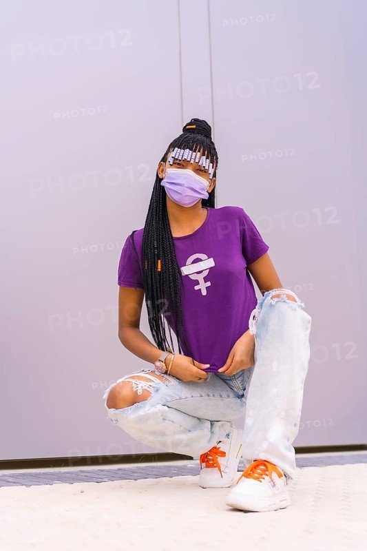 International women's day in the year of the coronavirus pandemic, covid-19. Dominican woman with feminist purple shirt and face mask, gray plain background