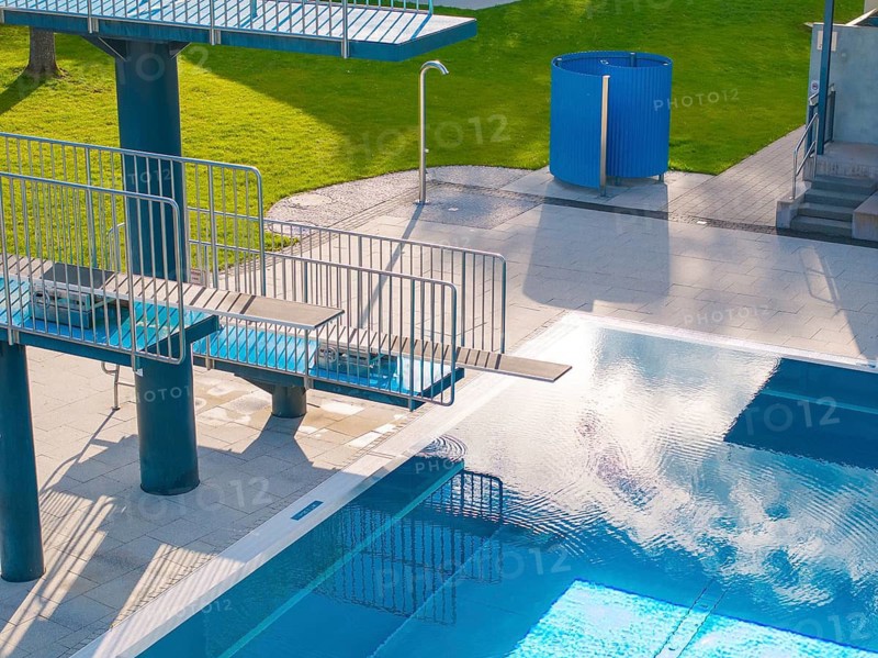Part of an outdoor pool with diving board and water reflections, adjacent to a green area, Calw Stammheim outdoor pool, Calw, Black Forest, Germany