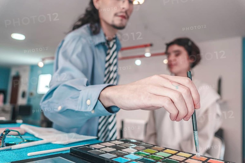 Professional makeup artist selecting an eyeshadow color from a diverse palette while preparing to apply makeup to a client in a modern beauty salon
