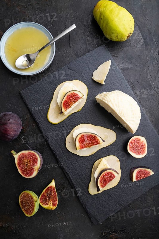Summer appetizer with pear, cottage cheese, figs and honey on slate board on a black concrete background. Top view, flat lay, close up