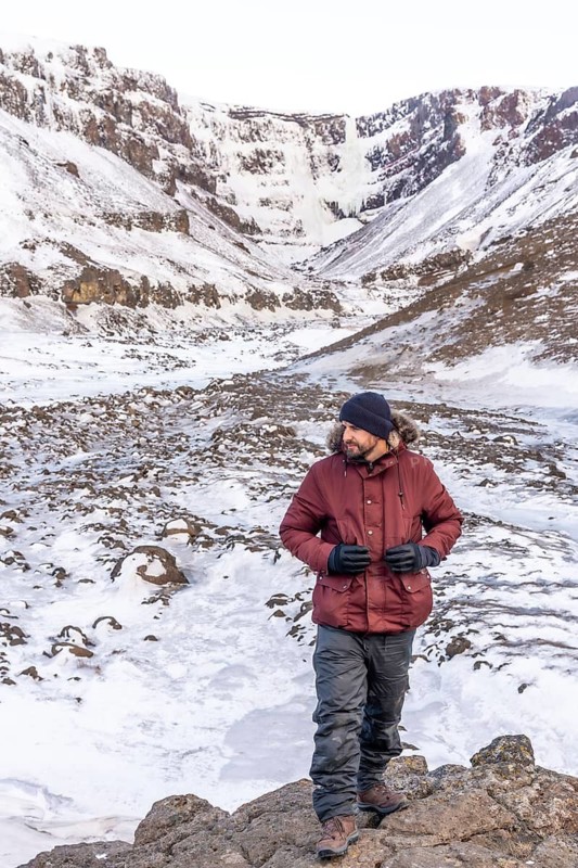 Portrait of a hiker at frozen Hengifoss waterfall in cold Iceland winter, volcanic cliffs
