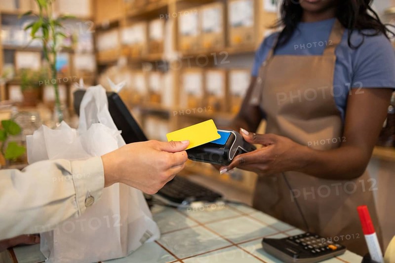 A store clerk in an organic supermarket assists a customer making a purchase with a card payment. Bulk items are visible in the background, emphasizing an eco-friendly shopping experience