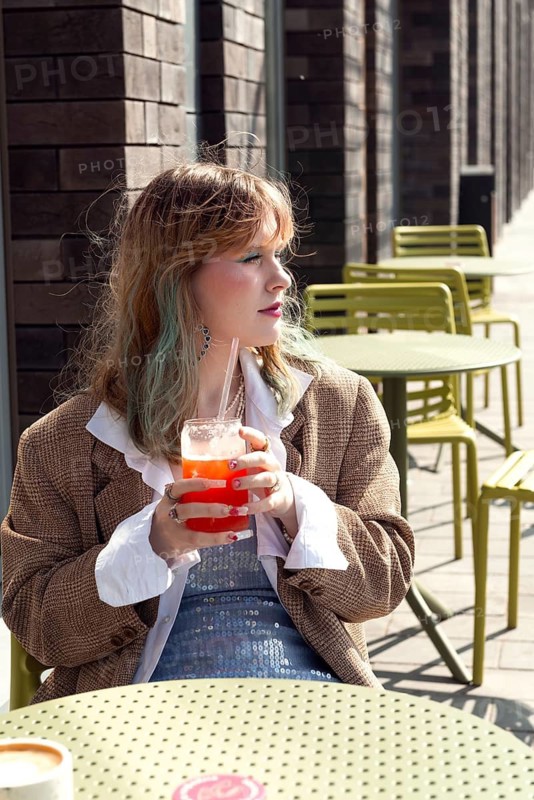 A woman with light hair sips a bright beverage at an outdoor cafe with colorful tables The stylish setting and sunlight create a vibrant, relaxed atmosphere