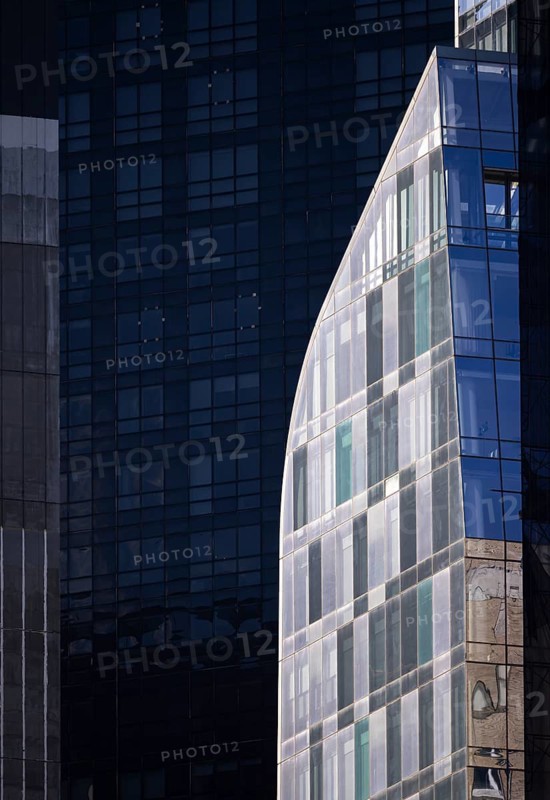 Modern glass building with curved design contrasts sharply against a backdrop of dark, reflective metallic towers in New York. The image captures the dynamic urban architecture and varied textures and colors of the city skyline