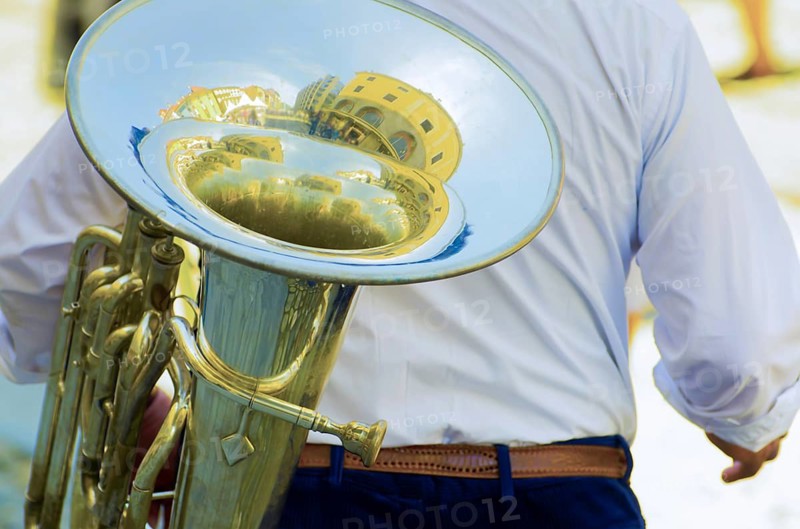 Man Carrying a French Horn Brass with Reflected House Inside His Music Instrument in a Sunny Day in Switzerland