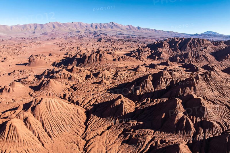 Stunning aerial view of the dramatic, sculpted terrain of Devil's Desert in Salta, Argentina. Rugged formations under a clear blue sky highlight the breathtaking natural beauty