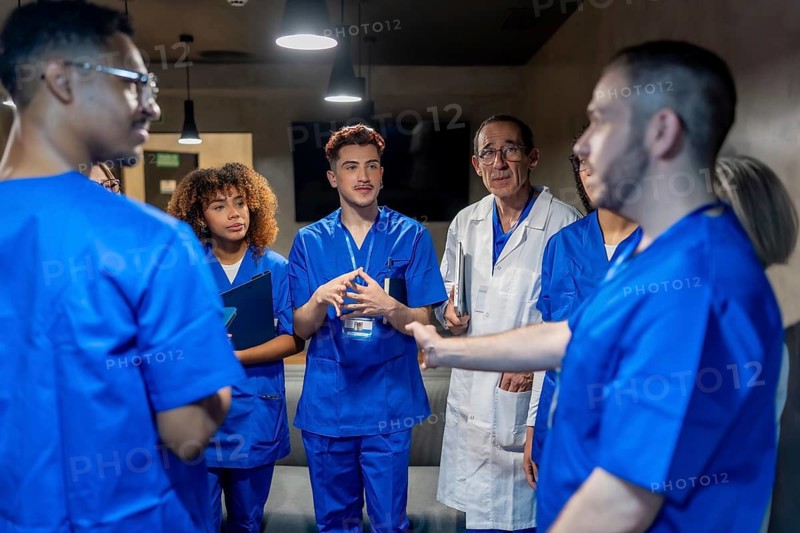 Diverse group of healthcare professionals wearing scrubs and lab coats engaging in a serious discussion, collaborating on patient care and hospital operations