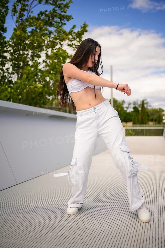Vertical photo of a cool young caucasian woman in white casual clothes dancing in an urban space