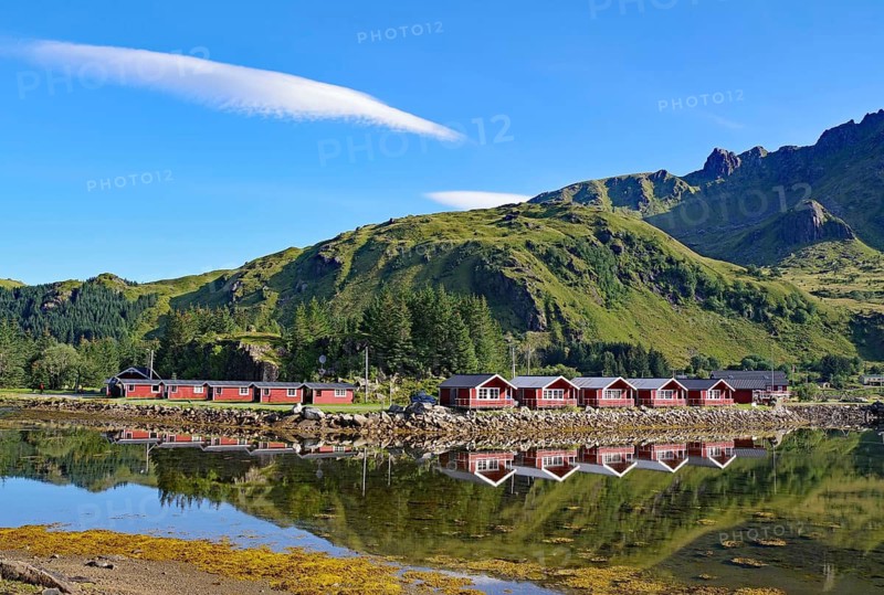 Red wooden cottages reflected in the water, green mountain landscape, Brustranda, Vestvågøy, Lofoten, Nordland, Norway