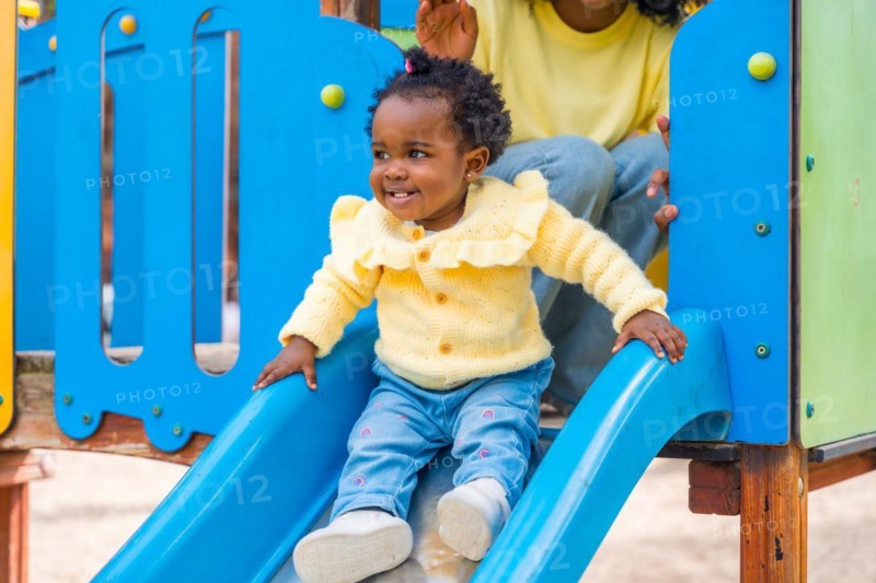 Adorable african girl having fun in a colorful slide next to her mother