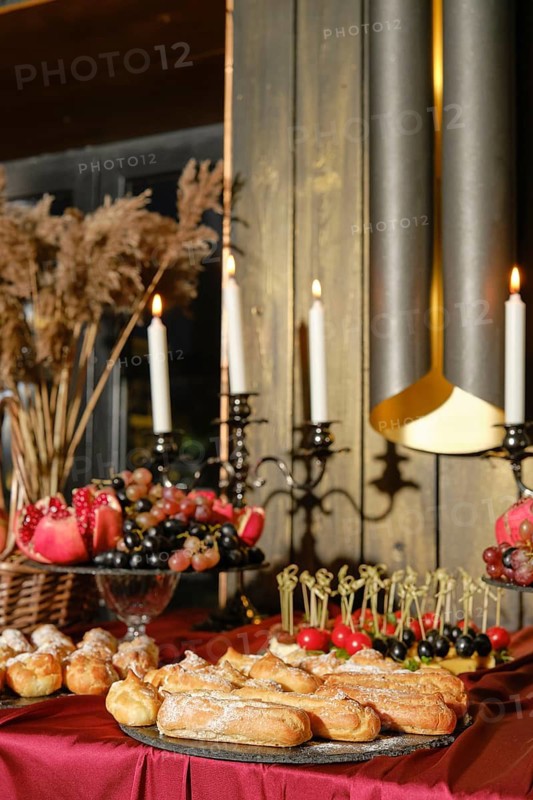 A beautifully arranged dessert table displays a variety of pastries, fruits, and decorative elements, complete with candles and plants, creating a warm atmosphere for a festive gathering