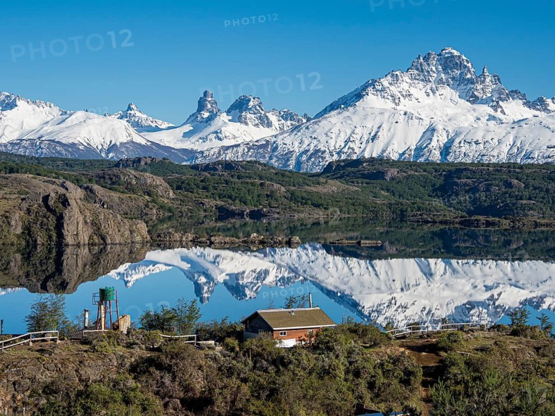 The snow-covered Mt. Cerro Castillo is reflected in a lake, small farm by the lake, Patagonia, Chile