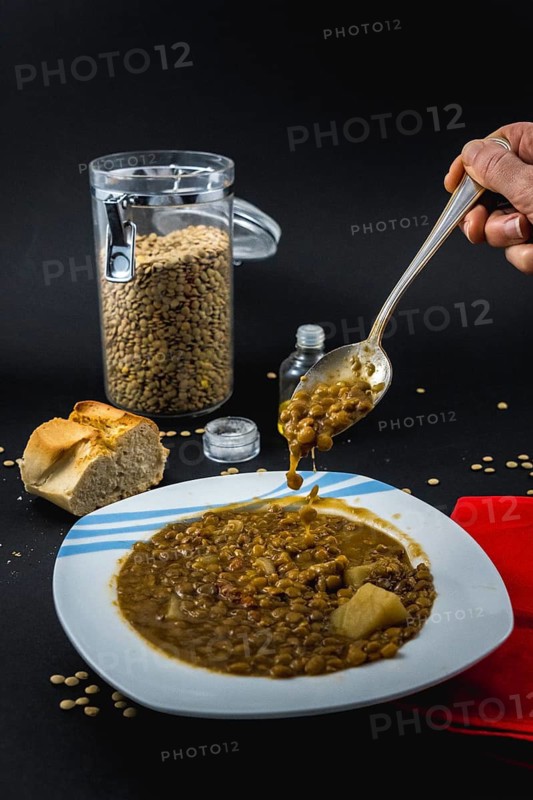 Eating with a spoon inside a plate of Spanish cooked lentils, along with ingredients salt and oil
