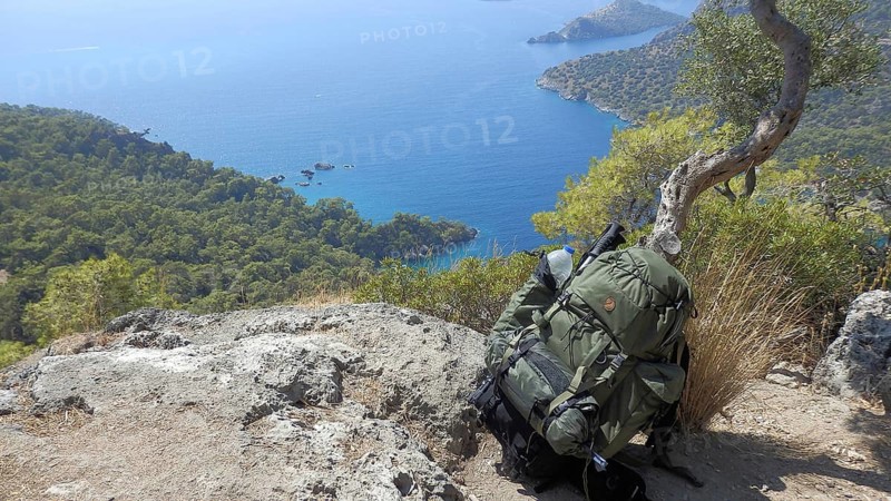 Rucksack leaning against a thin tree on a rocky slope with a view of the blue sea and trees, hiking the Lycian Way, Lycia, Turkey