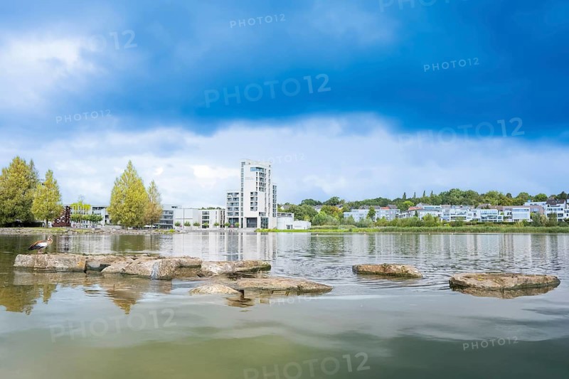 Phoenix Lake Dortmund, foreground water and the typical stone slabs or rocks, background houses, blue cloudy sky, Dortmund, North Rhine-Westphalia, Germany