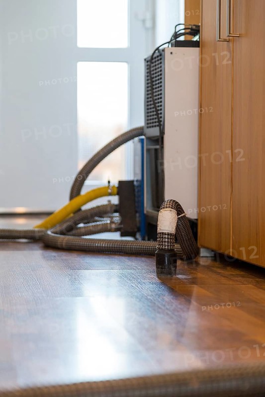 Professional water damage repair Drying equipment and hoses for underbody drying on wooden floor laminate