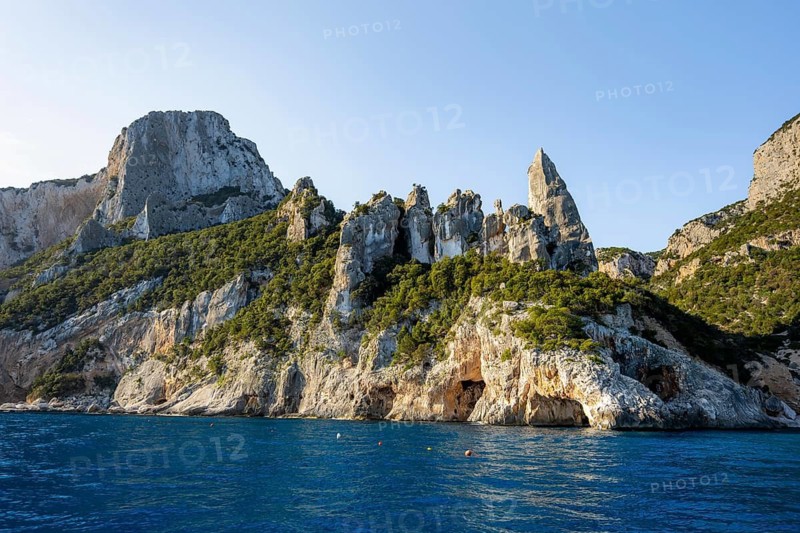Picturesque rocky coast, cliffs with caves in the morning light, L'Aguglia rock peak, blue sea and Cala Goloritzé beach, Golfo di Orosei, Baunei, Sardinia, Italy