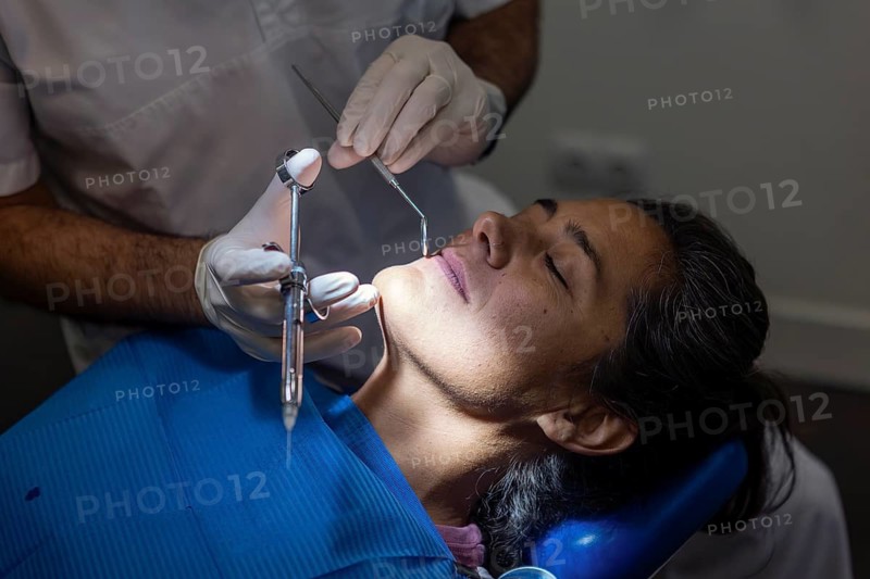 A dentist in gloves performs a teeth cleaning on a patient in a clinic. The dental chair and equipment are visible, highlighting a focus on oral health care