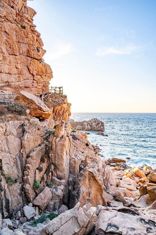 A little trail passing the rocks at the coastline with blue water at Costa Paradiso on a sunny day at sunset, Sardinia, Italy