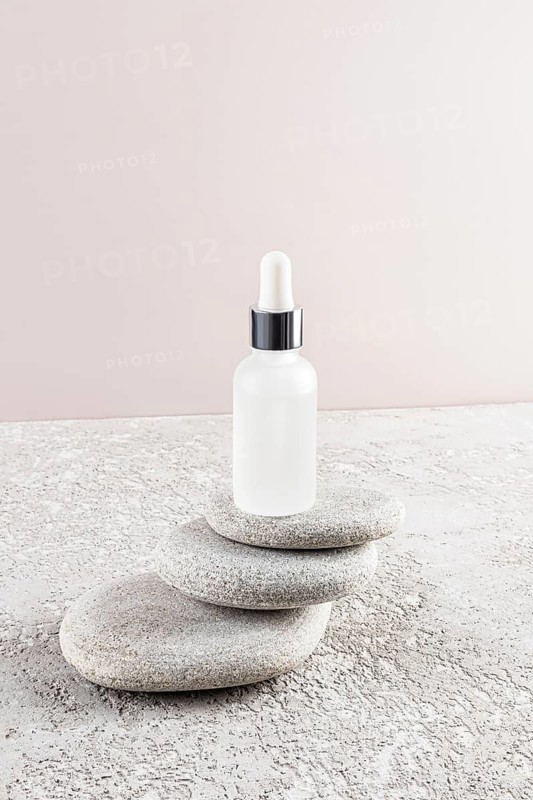 A minimalist scene of a frosted glass dropper bottle placed on smooth, stacked stones The neutral background emphasizes the elegance and simplicity of skincare packaging