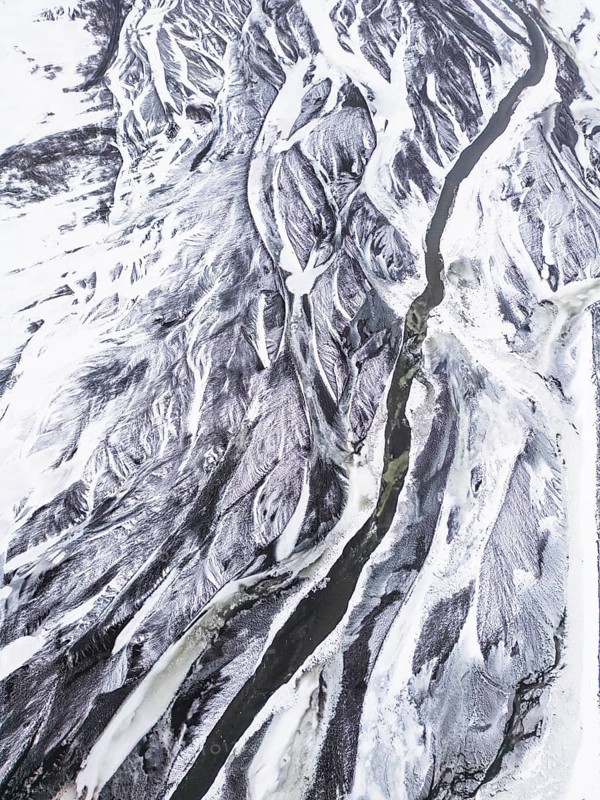 Aerial view of a snow-covered Icelandic winter landscape showcasing a winding river cutting through the rugged, icy terrain, highlighting nature's raw and remote beauty, VÃ­k Ã­ MÃ½rdal, SuÃ°urland, Islandia