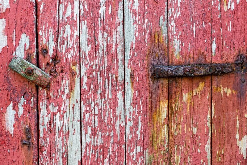 An old wooden door with peeling red paint and a rusty hinge, Mykines, Faroe Islands