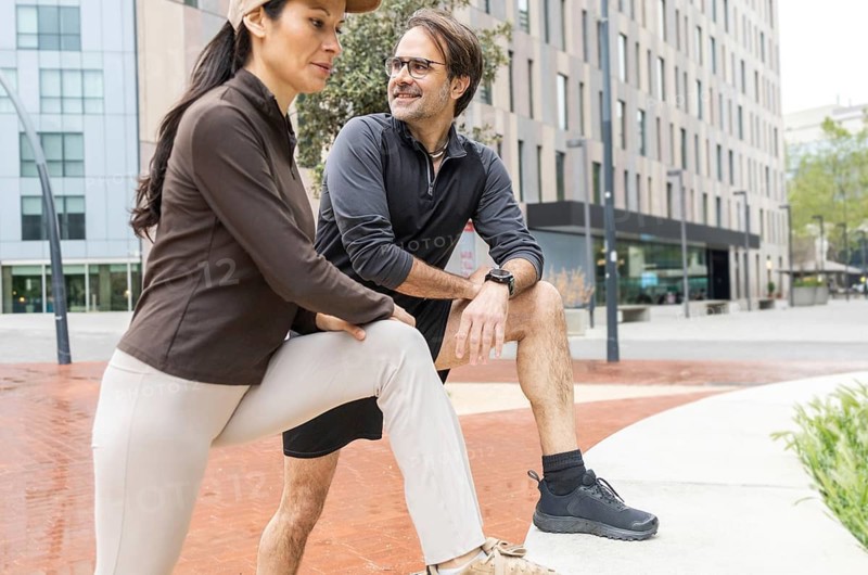 A couple engages in a stretching routine outdoors, preparing for a workout. The urban setting provides a modern backdrop, highlighting their active lifestyle and commitment to fitness