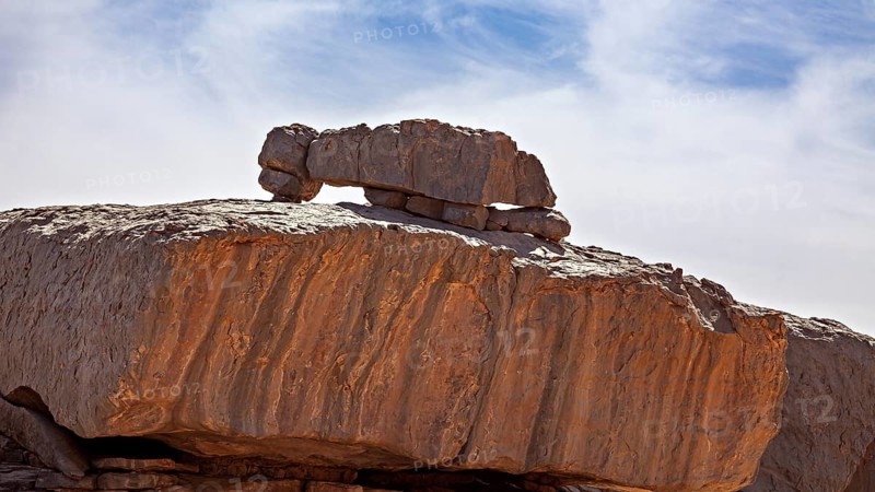 A balanced rock formation under a blue sky in a barren desert landscape, The man praying in front of Allah in a rocky landscape in the Sahara in Algeria